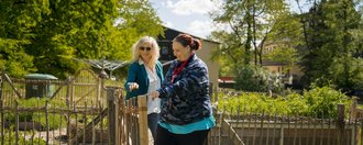 Zwei Frauen betreten den Garten durch das Gartentor.