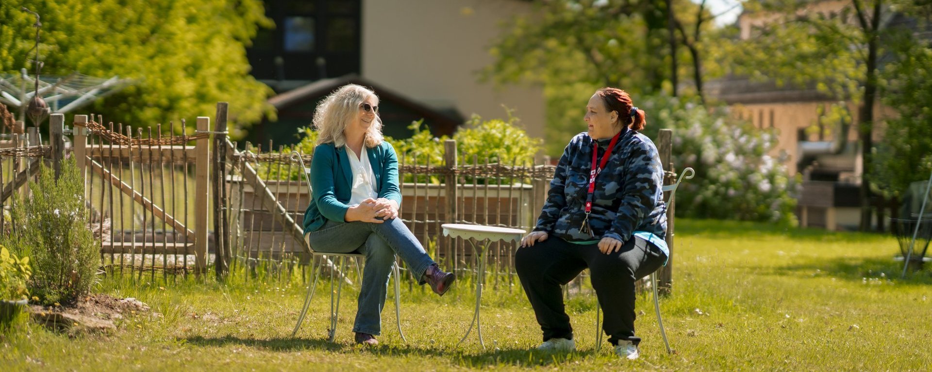 Zwei Frauen sitzen sich im Garten gegenüber und tauschen sich aus.